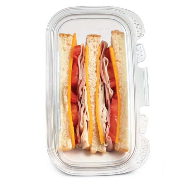 Layered deli meat and cheese sandwich with tomato slices in a glass container