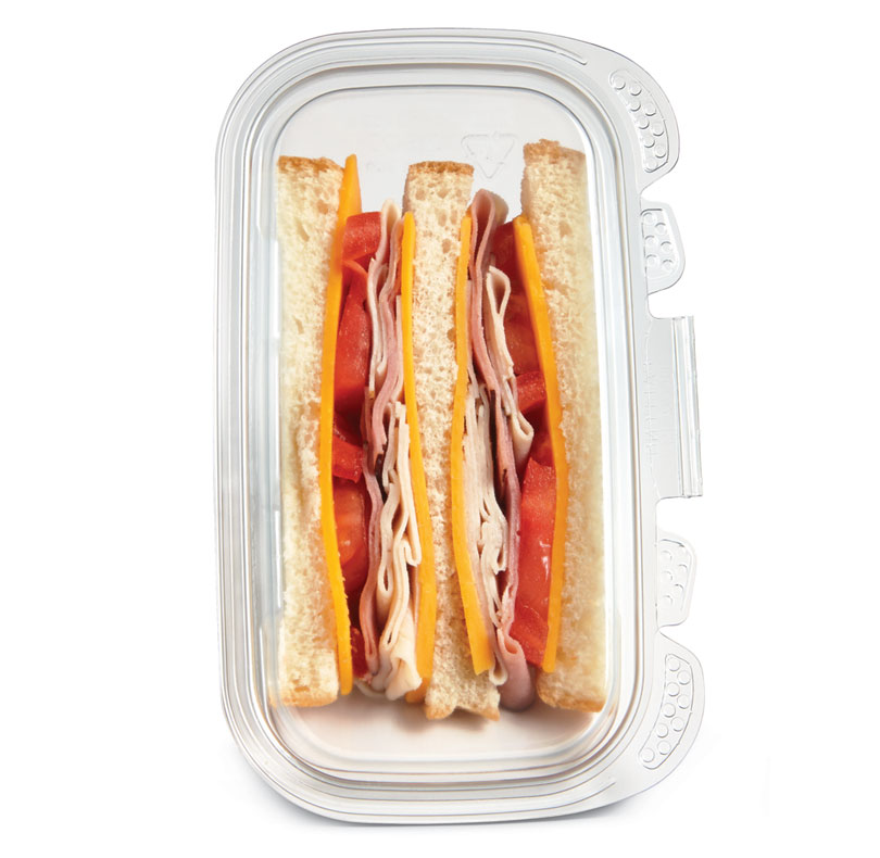 Layered sandwich with white bread, sliced ham, cheese, and tomato in a glass baking dish