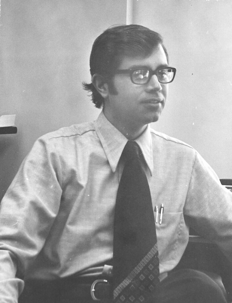 Black-and-white portrait of a man wearing glasses, a dress shirt, and patterned tie
