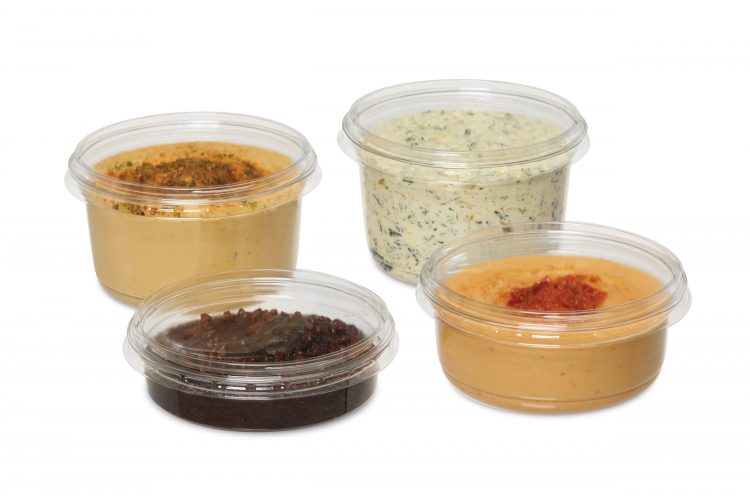 Four clear plastic containers holding assorted dips and spreads