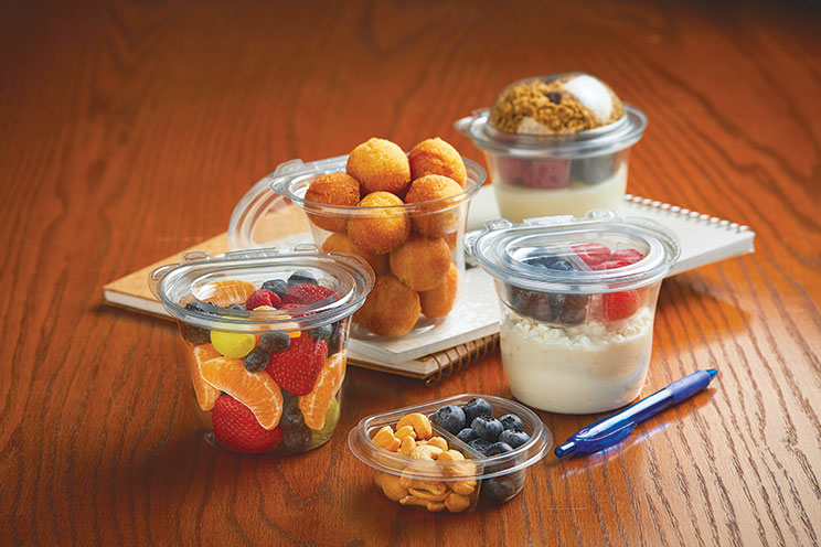 Several containers of fruit, granola, yogurt, and nuts arranged on a wooden table with a pen