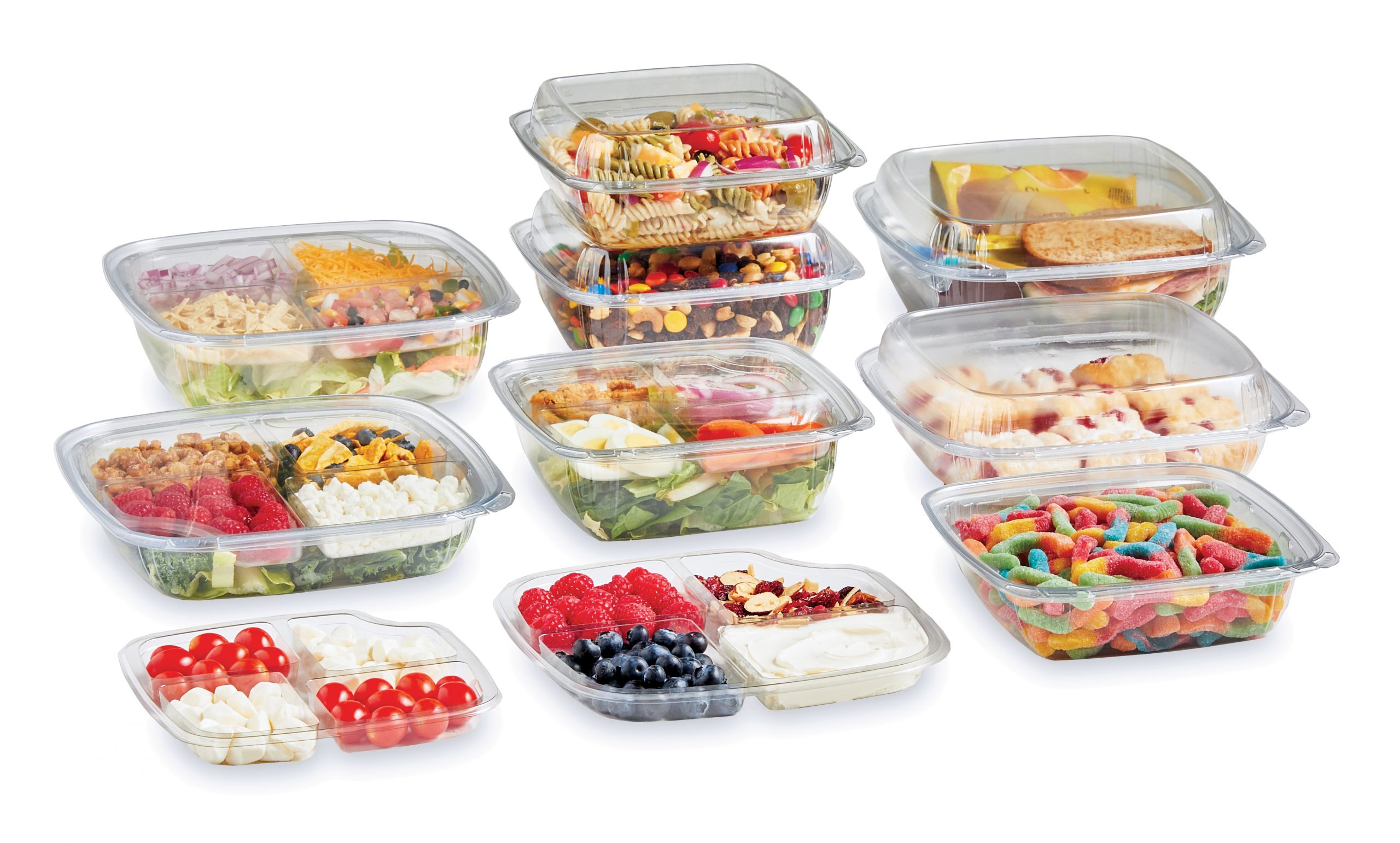 Assortment of clear compartmentalized food containers filled with salads, snacks, fruit, sandwiches, and candy