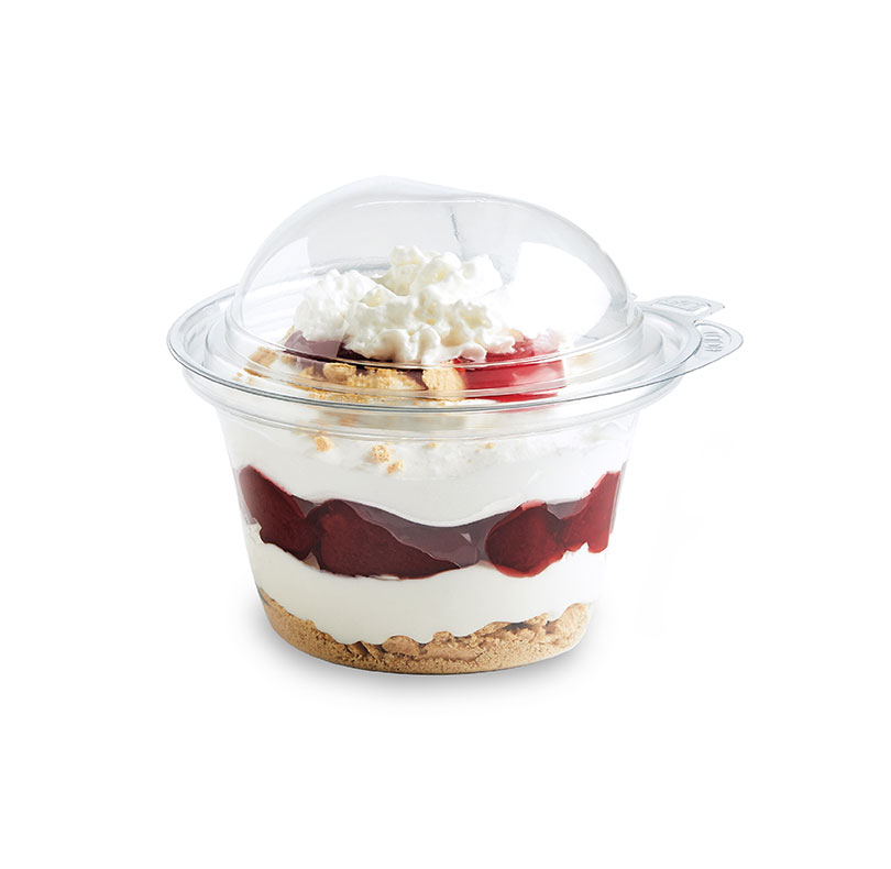 Layered berry cheesecake dessert in a clear cup, topped with whipped cream and cookie crumbs