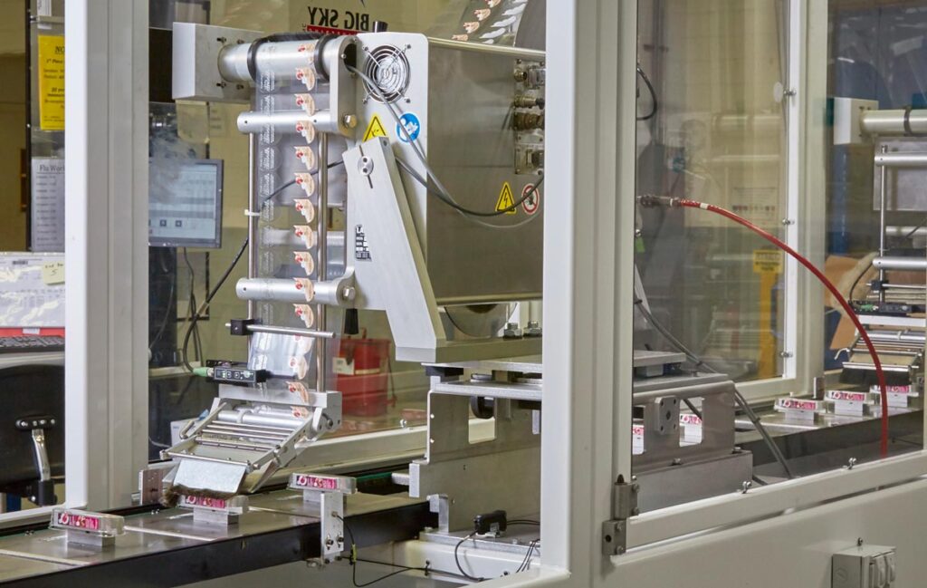 Automated packaging machine dispensing wrapped products onto a conveyor belt