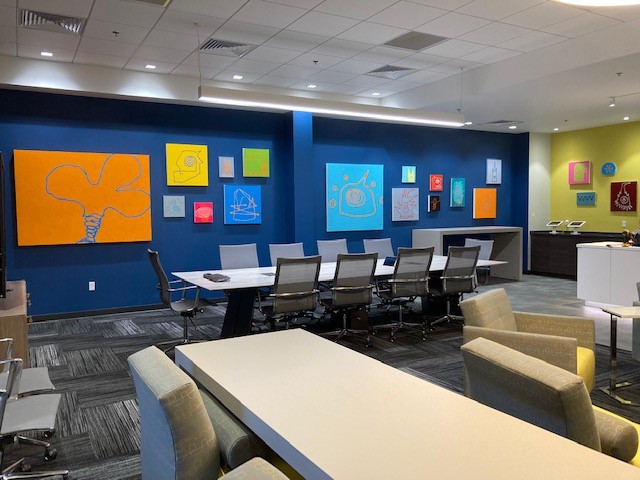 Modern office conference room with a long table, rolling chairs, lounge seating, and colorful artwork on blue walls