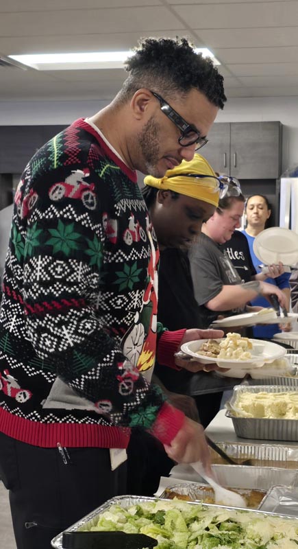 Careers 34 People serve food at a buffet, including a man in a Christmas sweater scooping salad onto a plate