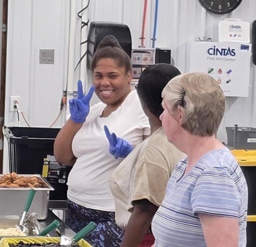 Careers 29 Three women in a food-service area, with a smiling worker in blue gloves making a peace sign