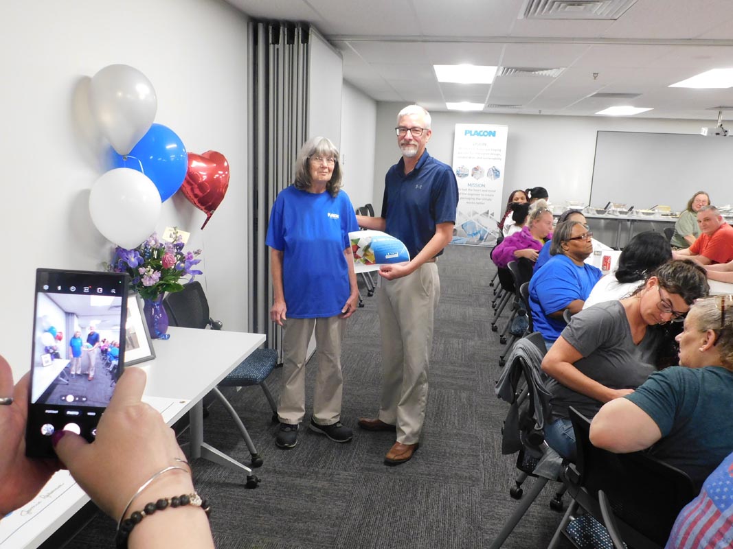 Careers 26 Two people pose at a gathering while a photographer captures them; attendees sit nearby and balloons decorate the room