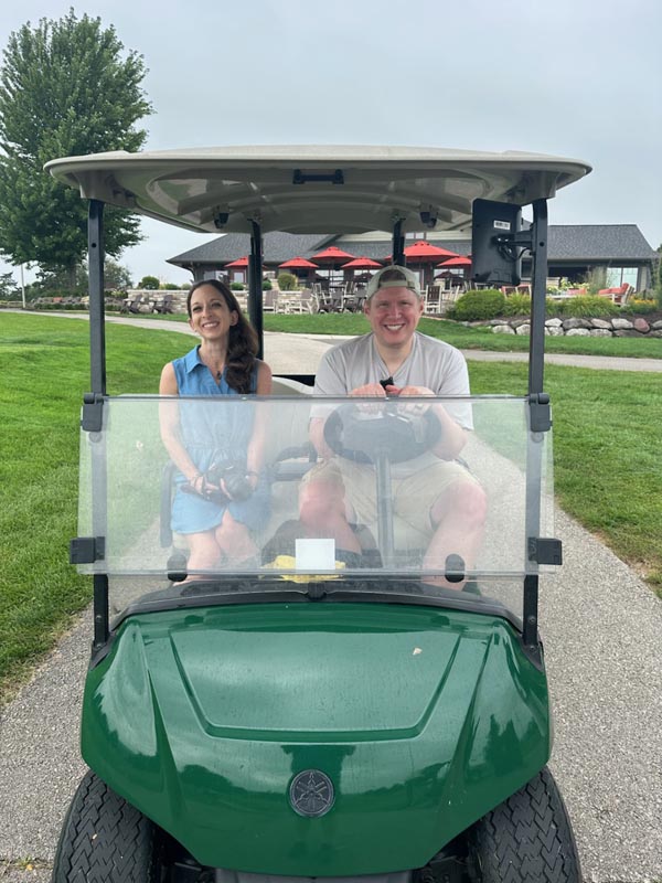 Careers 22 Two people smile while sitting in a green golf cart at a golf course