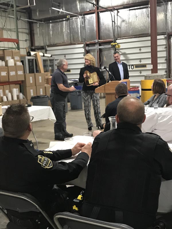 Careers 17 A woman holds a boxed item beside a podium as attendees watch during a gathering in a warehouse