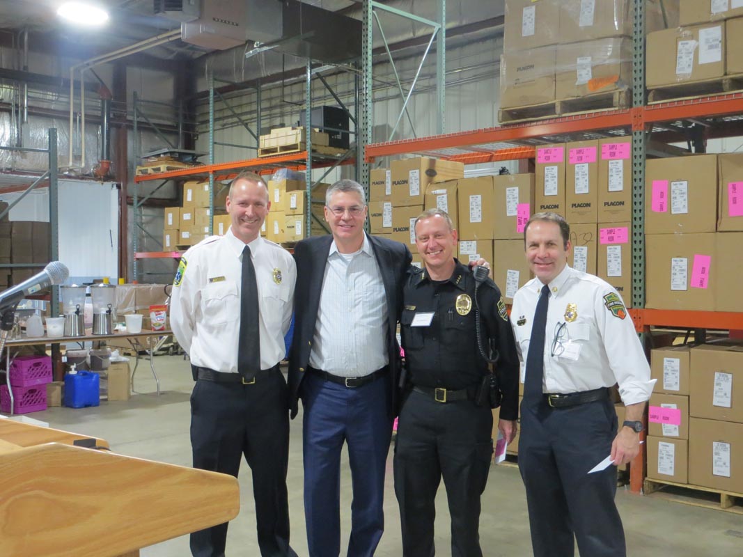 Careers 15 Four men, including three uniformed officers, stand in a warehouse in front of shelves stacked with cardboard boxes