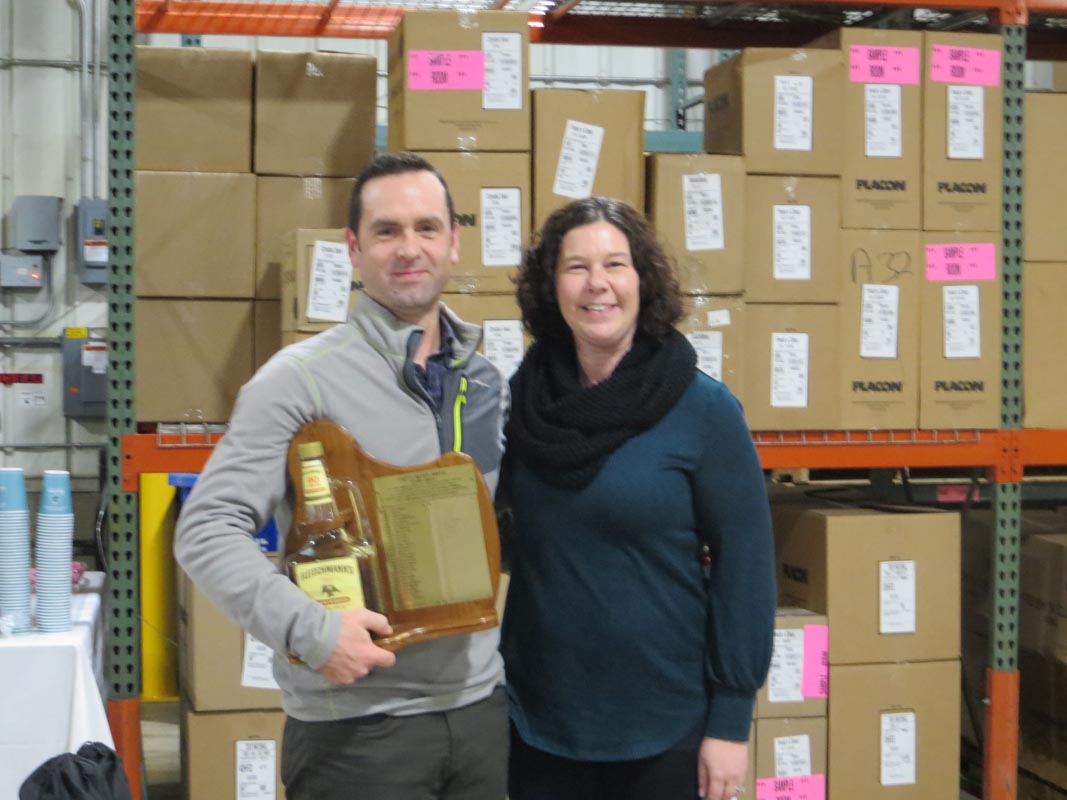 Careers 10 Two people pose in a warehouse; the man holds an award plaque with a bottle attached