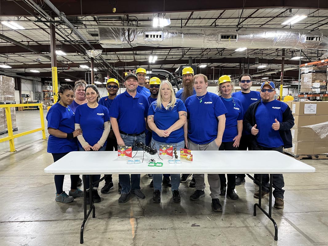 Careers 7 Employees in blue shirts and yellow hard hats pose behind a table in a warehouse