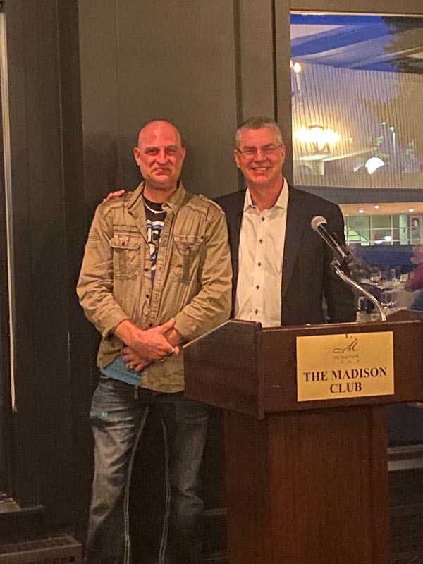 Careers 5 Two men stand beside a podium labeled “The Madison Club” in a banquet room